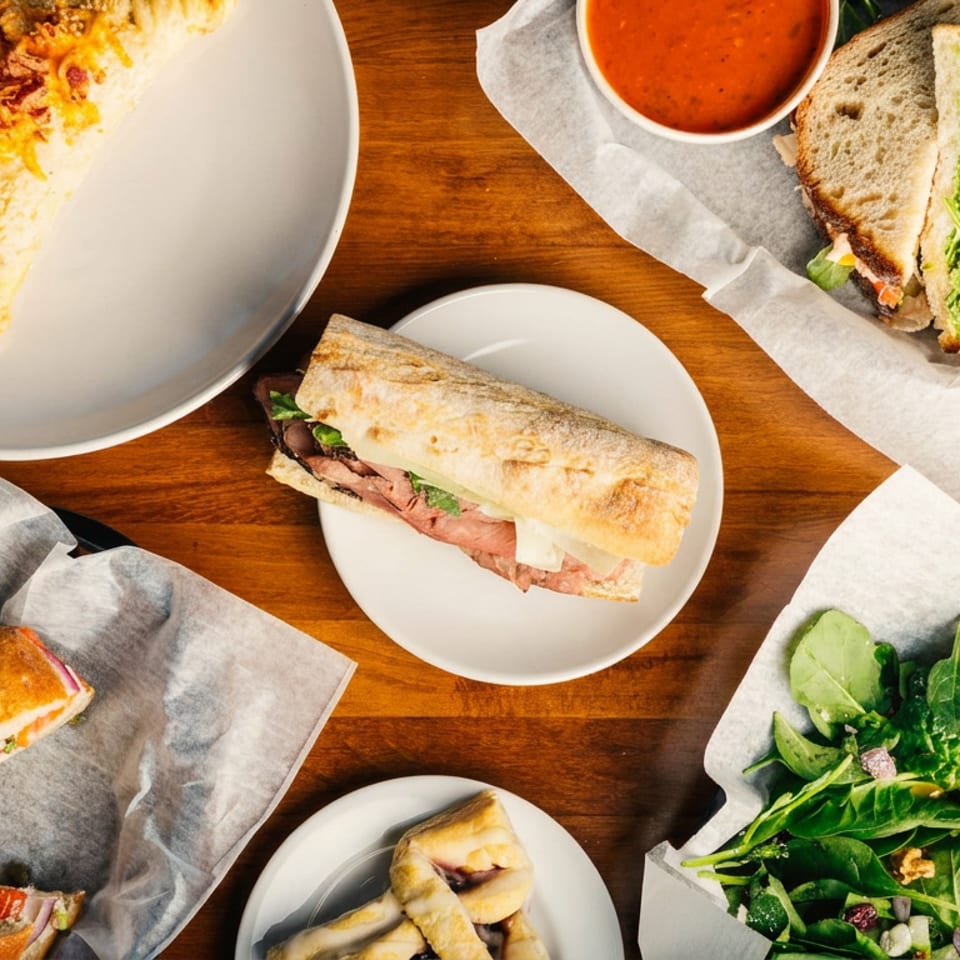 Assortment of sandwiches, pastries, salad, and soup on a wooden table.