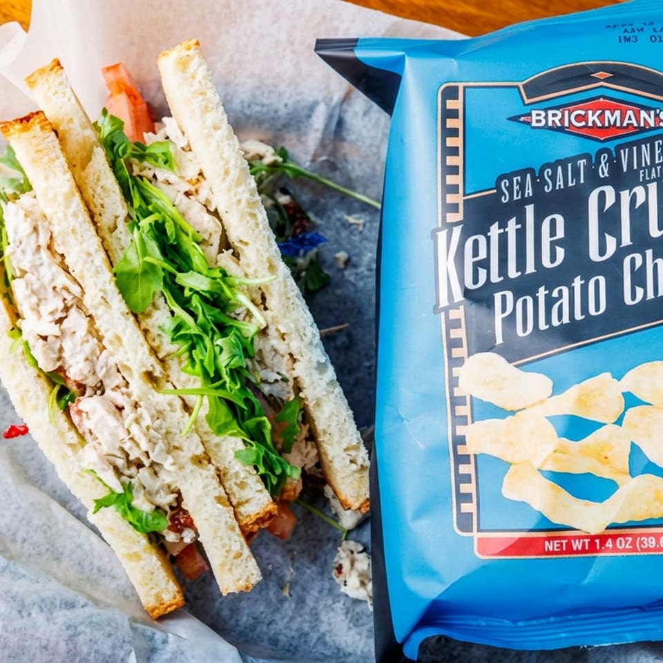 Chicken salad sandwich with arugula and a blue bag of Brickman's Sea Salt & Vinegar Kettle Crunch chips.